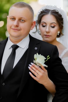 A man and a woman are posing for a picture. The man is wearing a black suit and tie, and the woman is wearing a white dress. They are both smiling and seem to be happy photo