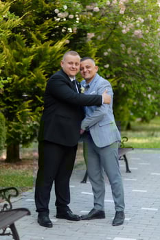 A man and a woman are posing for a picture in a park. The man is wearing a suit and tie, while the woman is wearing a dress. Scene is happy and celebratory photo