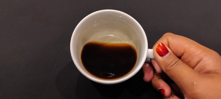 Women hand hold white cup with black coffee on black background. photo