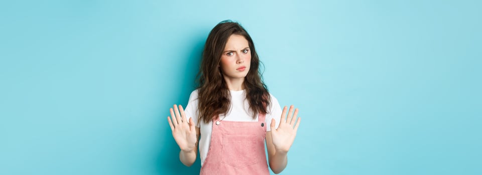 Stop right there. Serious young woman frowning, raising hands and showing block, say no, disapprove bad thing, rejecting you, standing against blue background photo