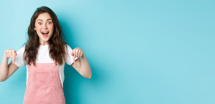 Wow so awesome. Excited cute girl telling big news, smiling amazed and pointing fingers down, showing cool advertisement, giving advice, recommending check out promo photo