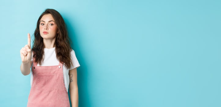 Rule number one. Serious young beautiful girl shaking finger in disapproval, scolding bad decision, make block or taboo gesture, standing against blue background photo