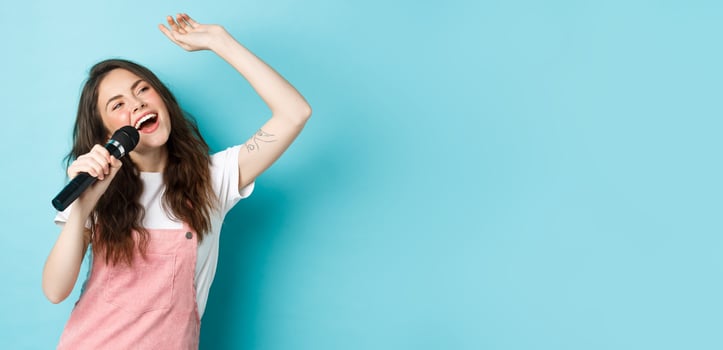 Beautiful female singer holding microphone, singing karaoke in mic, standing over blue background photo