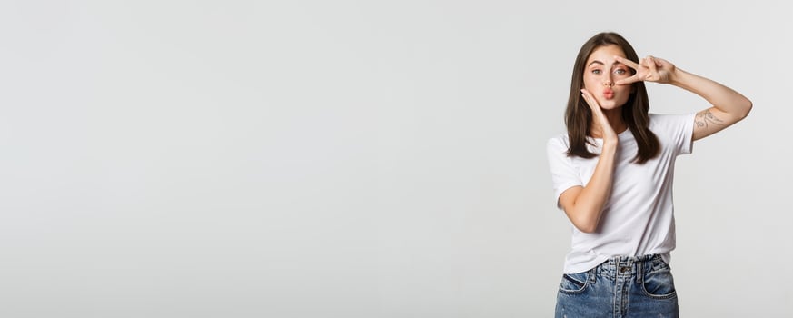 Beautiful young woman showing peace gesture and pouting silly, white background photo