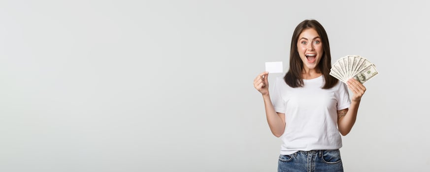 Excited happy brunette girl showing credit card and money, smiling over white background photo