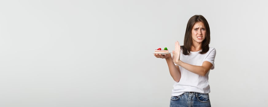 Disgusted young woman rejecting eating awful cake, making refusal gesture and grimacing displeased photo
