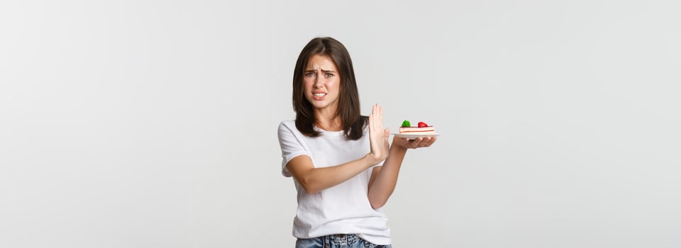 Disgusted young woman rejecting eating awful cake, making refusal gesture and grimacing displeased photo