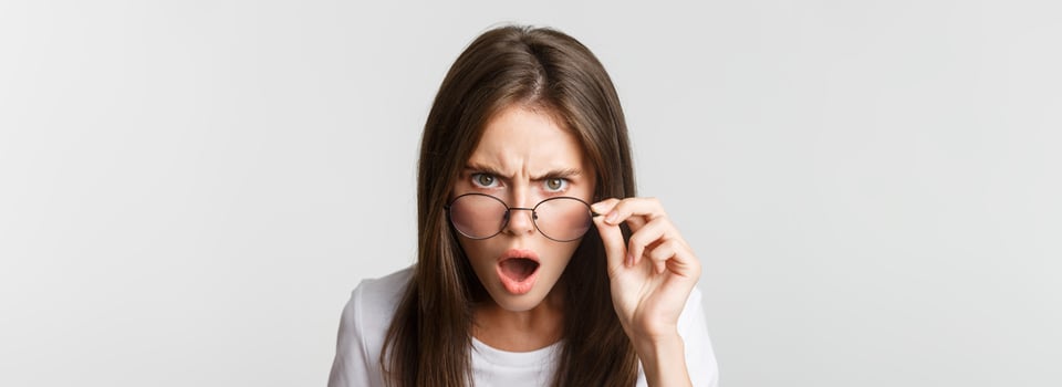 Close-up of insulted and shocked young angry woman looking from under glasses photo