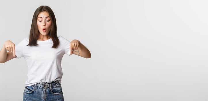 Intrigued attractive girl looking amused and pointing fingers down at logo photo