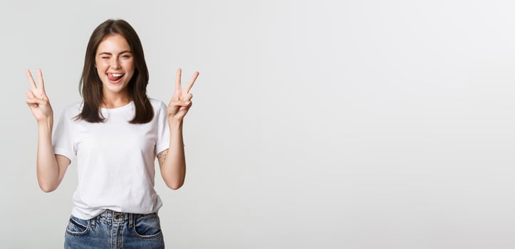 Cheerful cute brunette girl showing peace gestures and winking happy photo