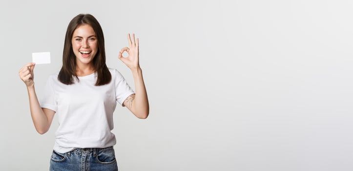 Satisfied attractive brunette girl showing credit card and okay gesture, recommend bank photo