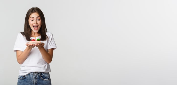 Excited attractive brunette b-day girl making wish on birthday cake, white background photo