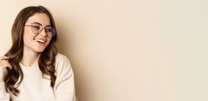 Close up portrait of stylish brunette woman in glasses, laughing and smiling, posing in eyewear against beige background photo