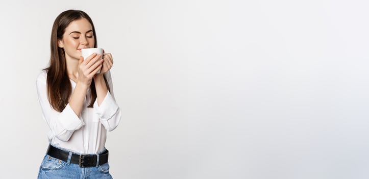 Smiling office woman drinking coffee, drink from mug with satisfaction, pleasure, standing over white background photo