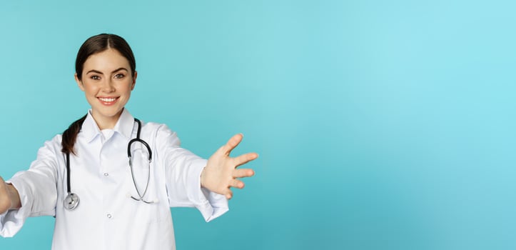 Smiling friendly doctor, girl healthcare worker, intern reaching hands, inviting, hugging or receiving in arms, standing over torquoise background photo