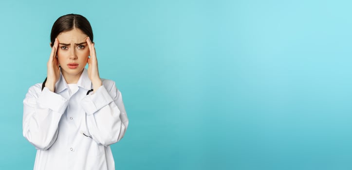 Image of woman doctor, medical personel grimacing from discomfort, having headache, migraine, feeling deezy, standing over torquoise background photo
