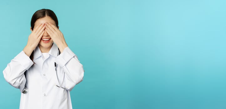Smiling happy therapist, woman doctor cover close eyes with hands and waiting for surprised, anticipating, standing in white coat over torquoise background photo