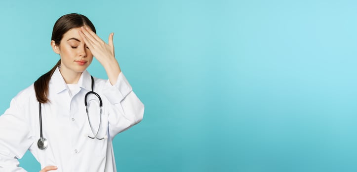 Portrait of annoyed, tired woman doctor, facepalm, roll eyes frustrated, bothered by smth stupid, standing in white coat over torquoise background photo