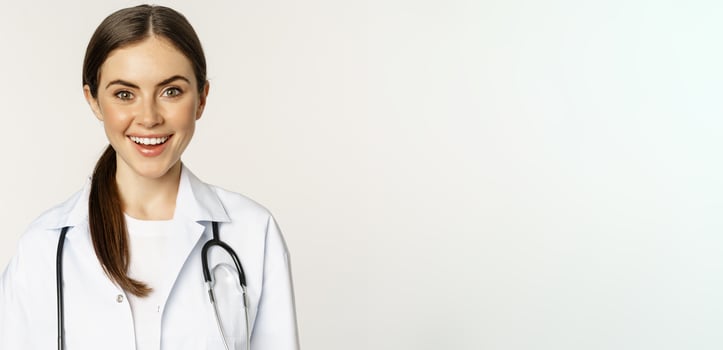 Smiling woman doctor, physician at appointment, looking happy and confident, wearing white coat and stethoscope, standing against studio background photo