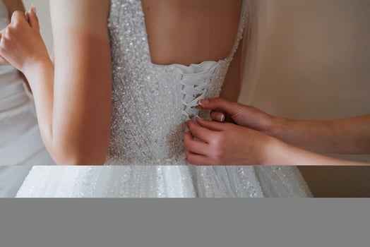 A woman is getting her dress altered by another woman. The dress is white and has a lot of sparkles photo