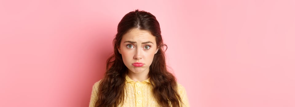 Close up of cute and coy girl making sad pouting face to ask for something, wants pity, standing against pink background gloomy photo