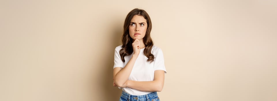 Portrait of serious woman thinking, looking up with indecisive thoughtful face, pondering, standing over beige background photo