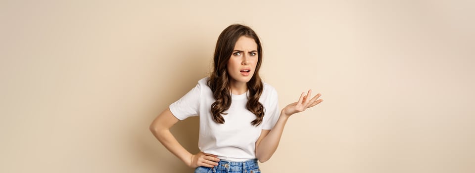 Confused woman looking clueless and annoyed, cant understand, asking whats problem, standing over beige background photo