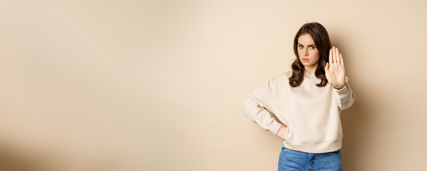 Stop. Serious and confident woman showing extended arm palm, prohibit, forbid smth, blocking something, standing over beige background photo