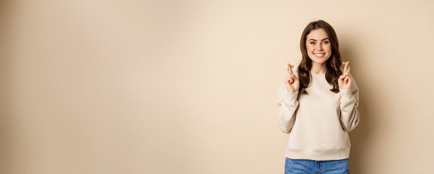 Confident woman praying, making wish with fingers crossed for good luck, standing over beige background photo