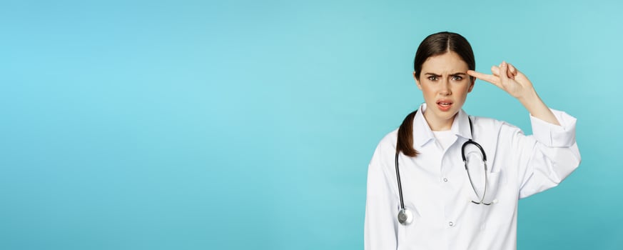 Annoyed woman doctor pointing finger at head, scolding someone stupid, crazy or strange, standing over torquoise background photo