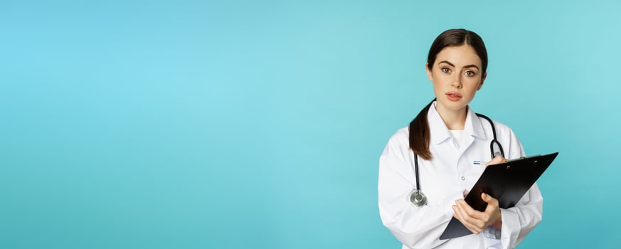 Image of professional woman doctor, physician with clipboard writing, listening patient at hospital clinic appointment, standing over torquoise background photo