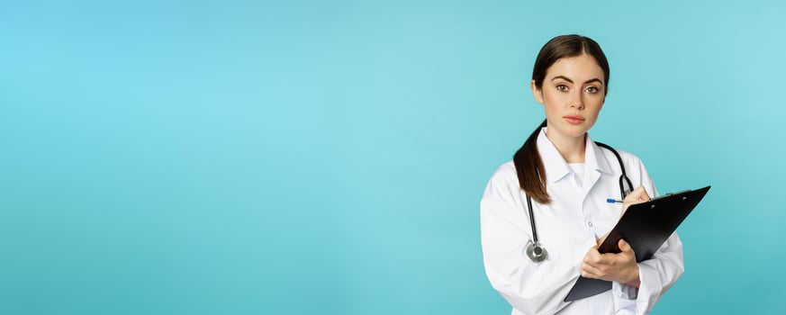 Image of professional woman doctor, physician with clipboard writing, listening patient at hospital clinic appointment, standing over torquoise background photo