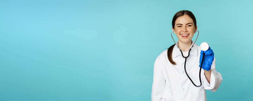 Image of woman doctor, listening patient lungs with stethoscope, doing medical checkup in clinic, standing over blue background photo