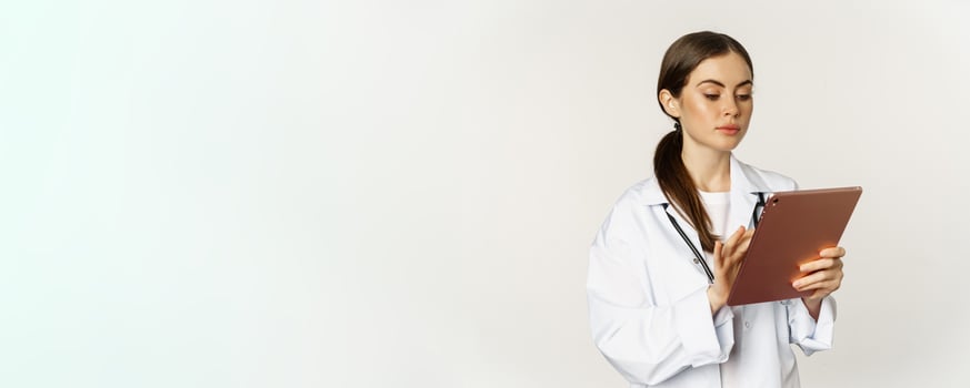 Doctor in white coat using digital tablet, reading medical data on gadget, working in hospital, standing over white background photo