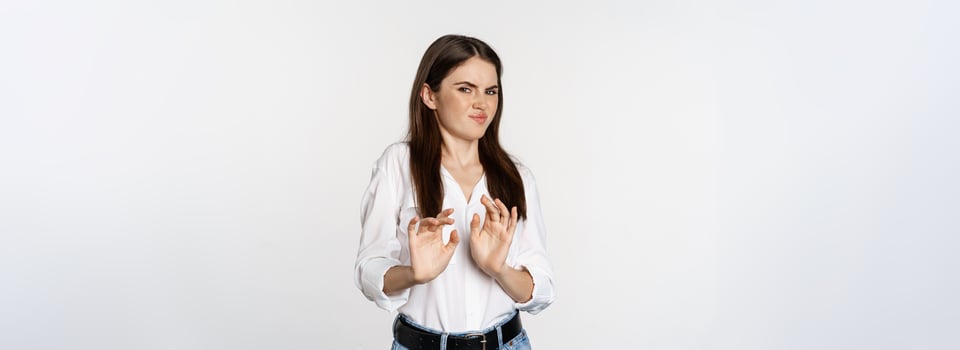 Displeased woman showing stop, rejection gesture, waving hands to decline, refuse of something ugly, standing over white background photo