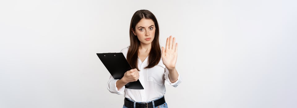 Serious woman with clipboard documents, extending arm, showing taboo stop sign, disapprove, prohibit smth, standing over white background photo