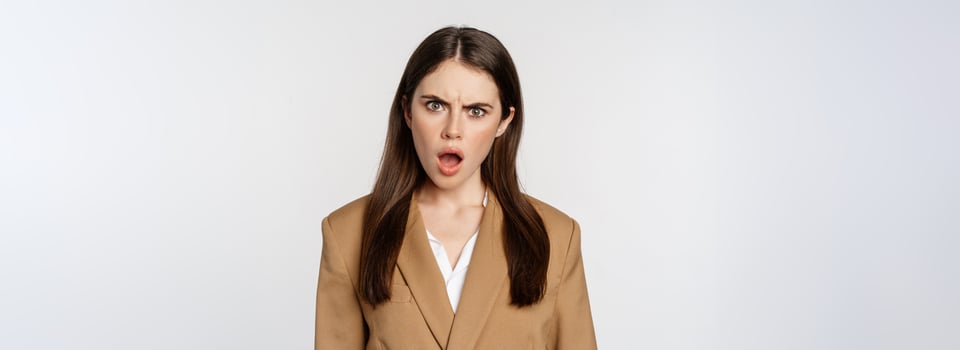 Frustrated, insulated woman in business outfit, staring startled and shocked at camera, standing over white background photo