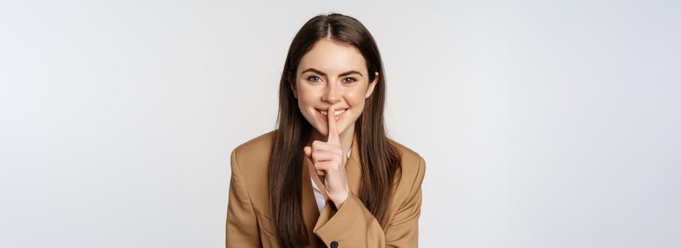 Close up portrait of female entrepreneur smiling, shushing, making shh hush sign, press finger to lips, tell secret, standing over white background photo