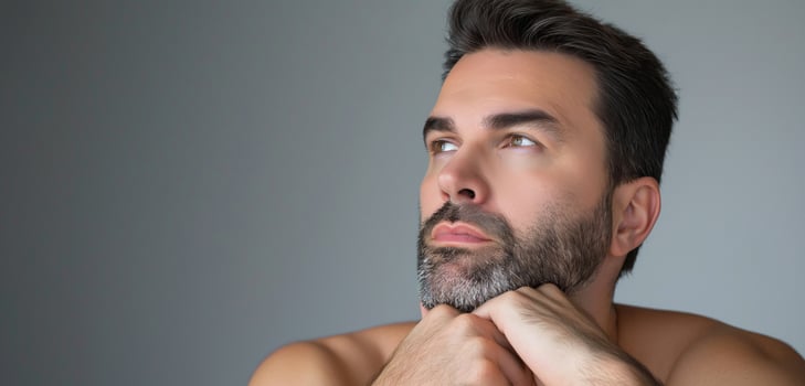 Contemplative Bearded Man Reflecting Indoors Against Neutral Background - Close-Up Thoughtful Expression photo