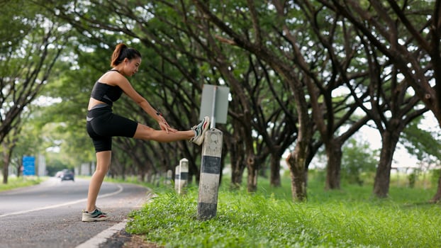 A woman is stretching her leg on a sidewalk next to a pole photo