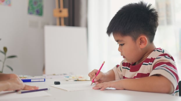 A boy is writing with a pink pencil on a piece of paper photo