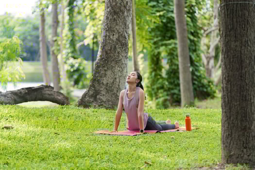 Woman Practicing Yoga and Relaxing in a Serene Park Setting with Lush Greenery and Trees photo