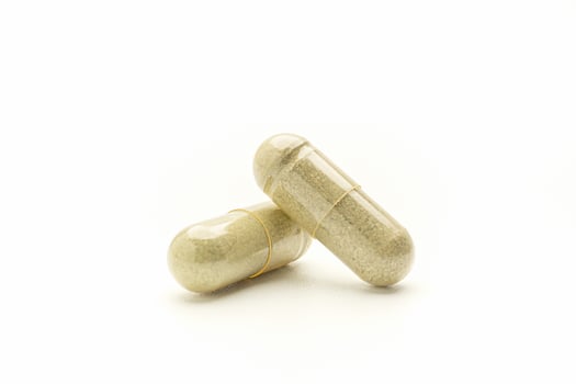 Close-up of Andrographis paniculata capsules placed isolated on white background. Space for text. Herbal, medicine, and healthcare concept photo