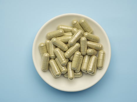 Close-up of Andrographis paniculata capsules are in a dish isolated on blue background. Space for text. Herbal, medicine, and healthcare concept photo