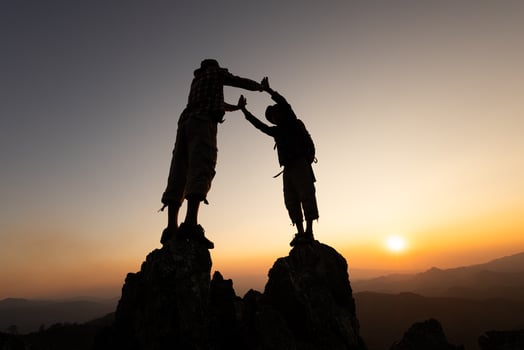 Silhouette of two climbers holding hands on the mountaintop represents success and unity, teamwork, photo