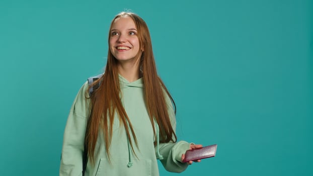 Jolly teenage woman holding passport, going on adventure trip, looking around. Cheerful wanderlust tourist backpacking, sightseeing, visiting attractions, isolated over studio backdrop, camera A photo