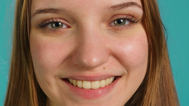 Extreme close up shot of cheerful joyous girl smiling, isolated over blue studio background. Portrait of happy upbeat teenager grinning, having positive facial expression photo