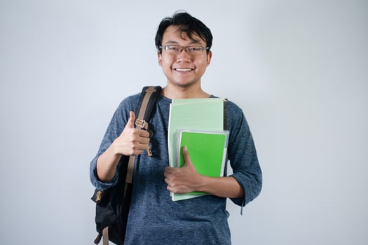 Asian young male student wearing bag and holding book smiling and happy expression. Ok hand sign gesture with isolated white background photo