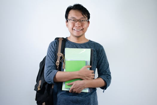 Asian young male student wearing bag and carrying books smiling and happy expression with isolated white background photo