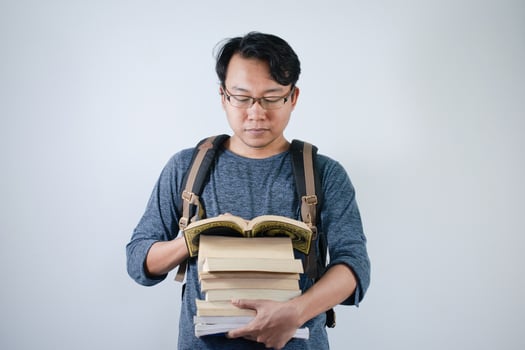 Asian young male student wearing bag and carrying a lot of books smiling and happy expression with isolated white background photo